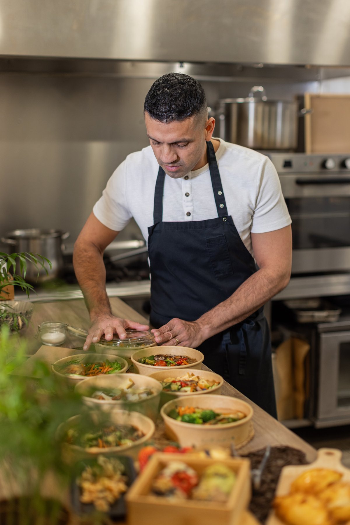 A chef in a professional kitchen carefully prepares and packs meals in eco-friendly bowls with fresh ingredients