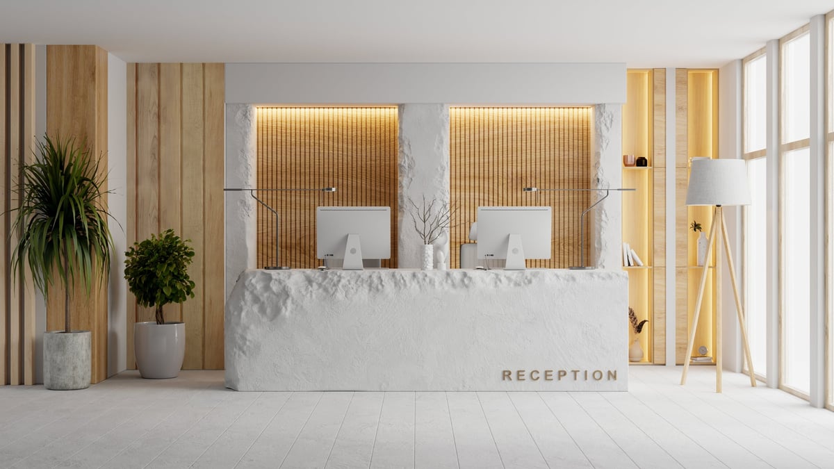 A stylish modern hotel reception interior featuring a white stone counter, wooden wall accents, and minimalist decor